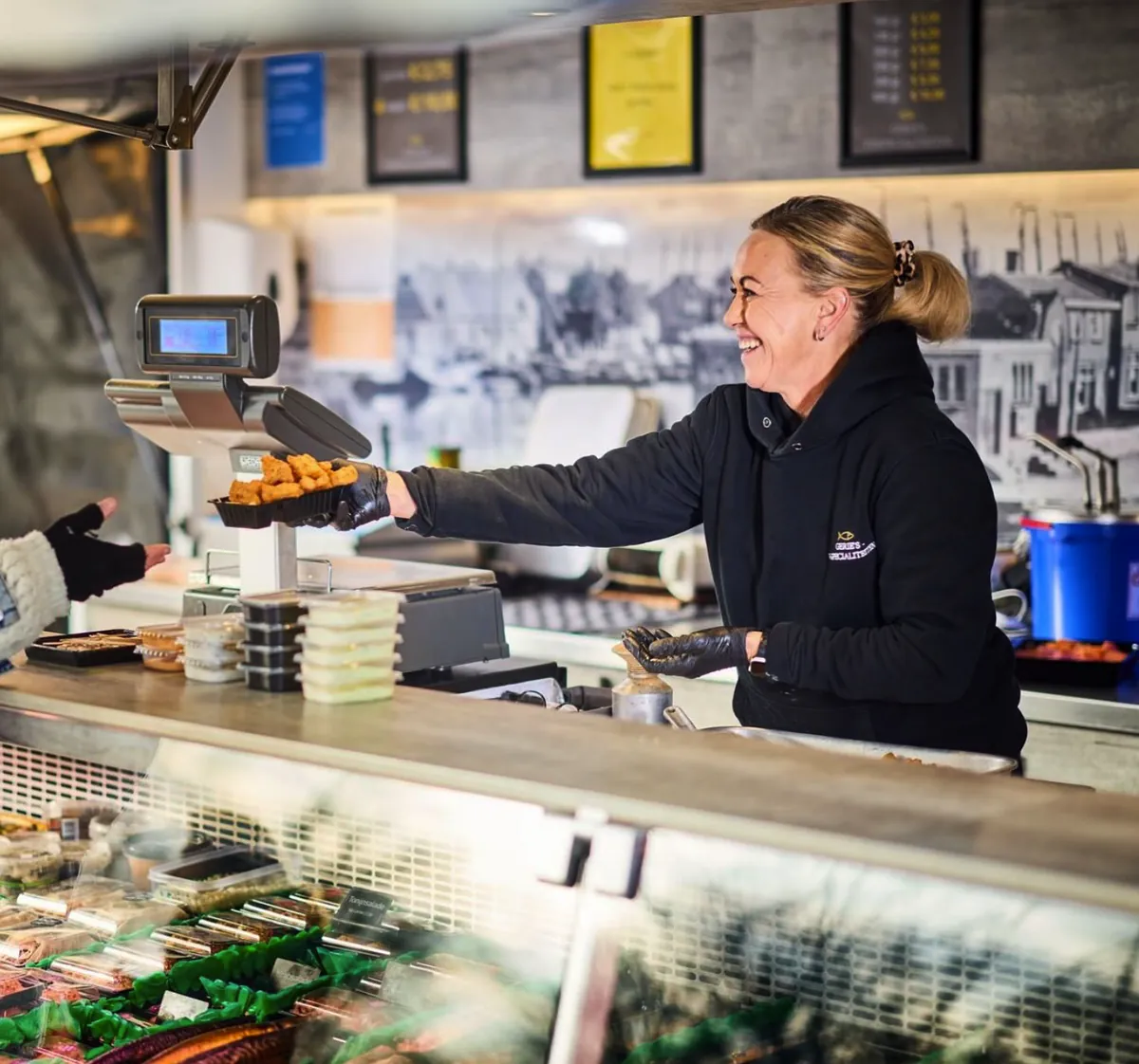 Een medewerkster van Gerie's geeft met een glimlach een bakje warm gebakken vis aan een klant